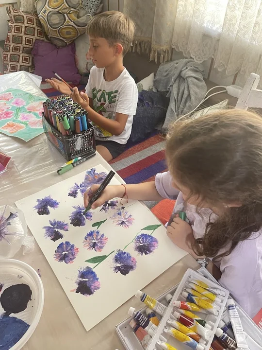 Children painting together at a shared table — from the world of Jasmina and PAGANE